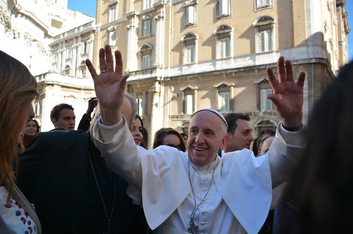 A man in a white robe is waving at a crowd of people.