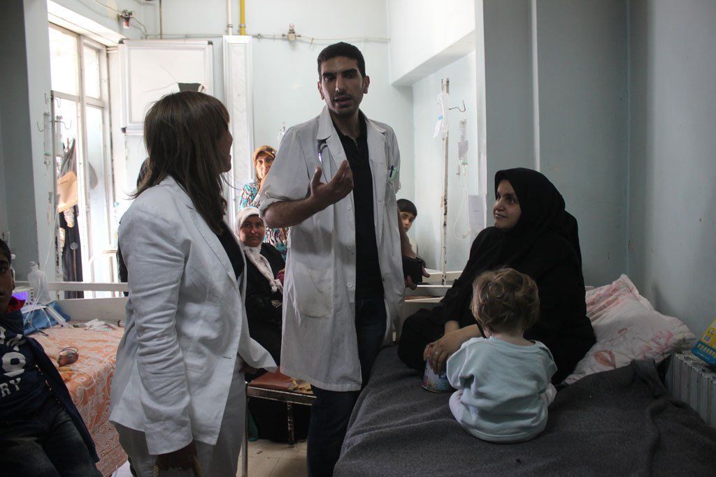 Two doctors talking with a patient as her child plays in Aleppo, Syria.