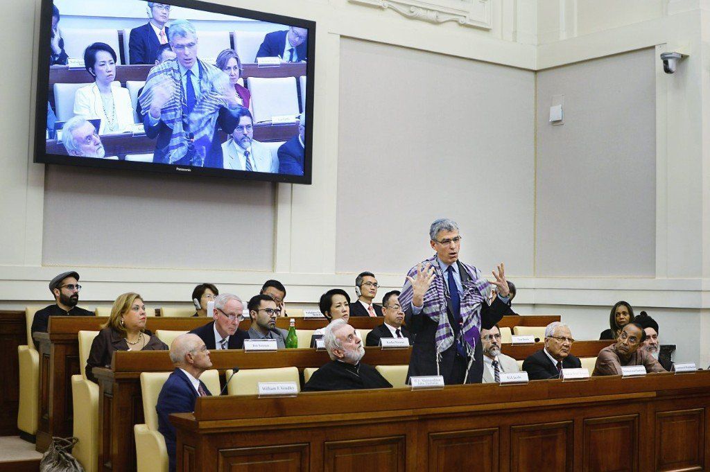 A group of people are sitting in a classroom with a large screen behind them.