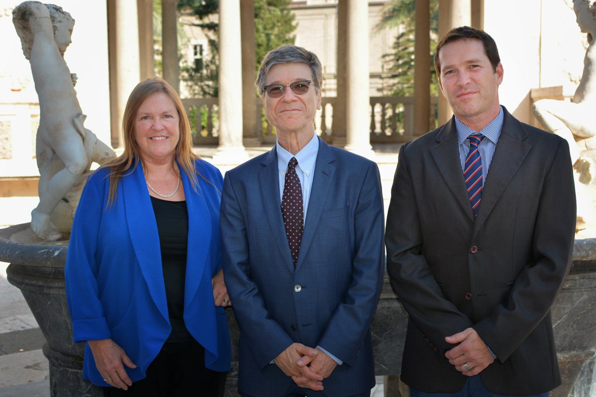A woman in a blue jacket stands between two men in suits