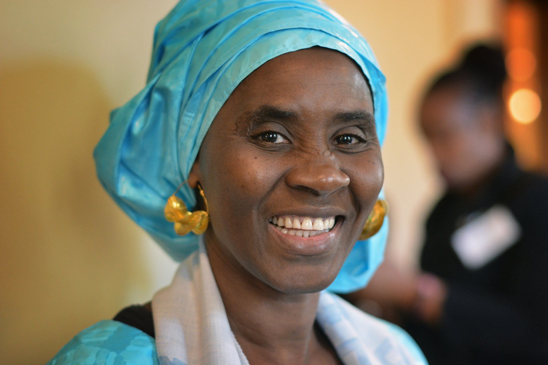 A woman wearing a blue turban and gold earrings smiles for the camera.