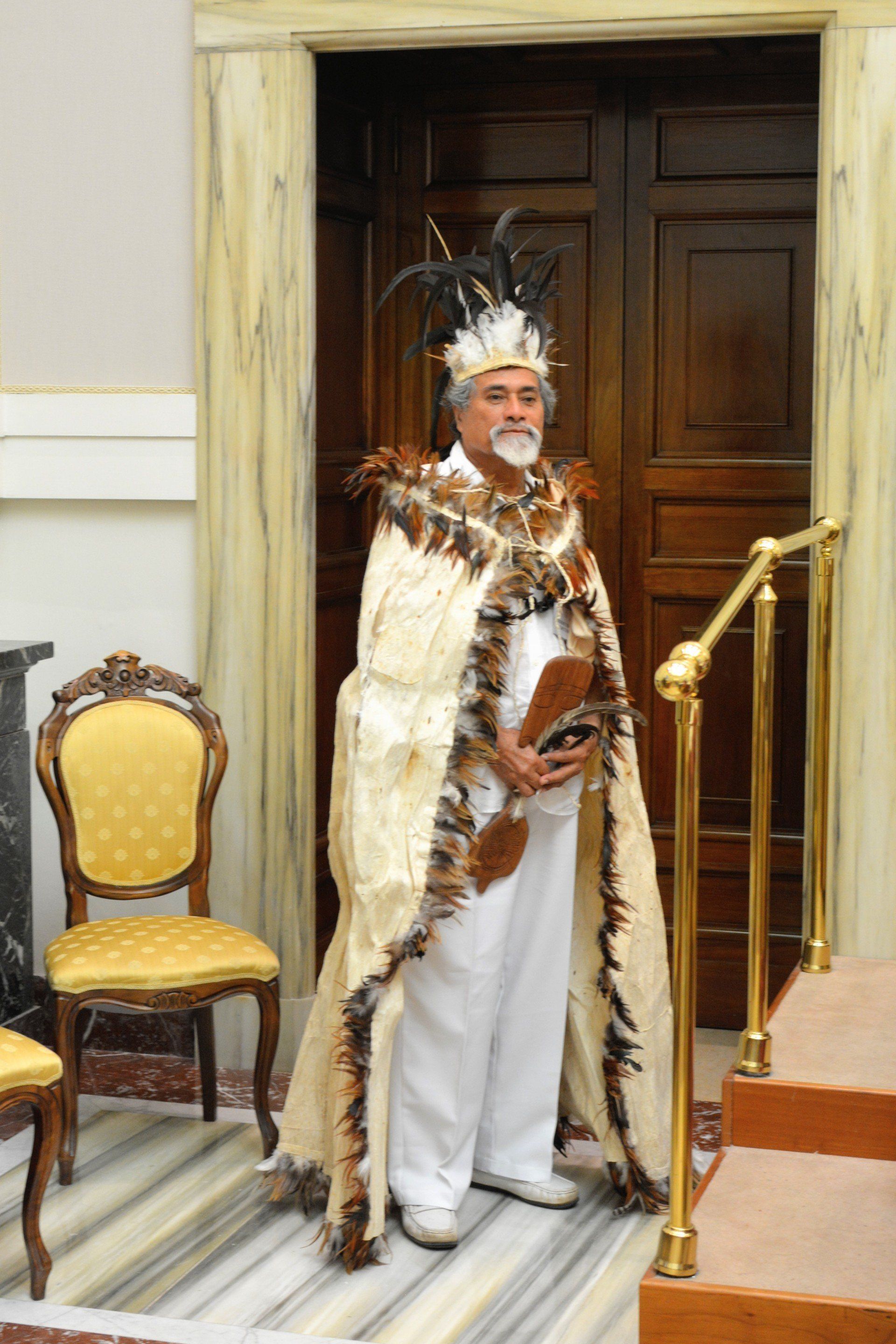 An indigenous man standing in a door way wearing a head dress and cape