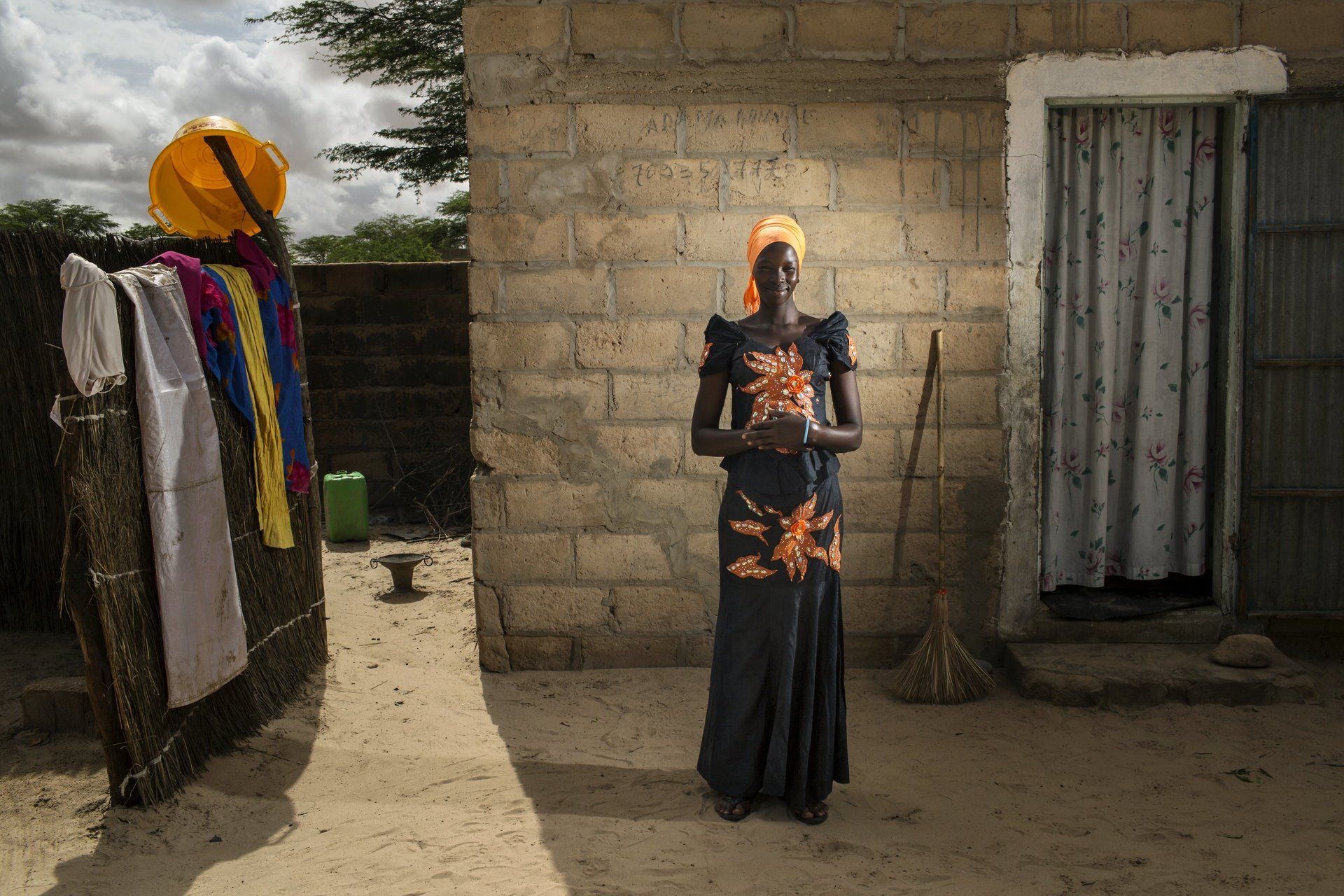 VII Foundation: A women in an orange and black dress standing in front of her home in her village