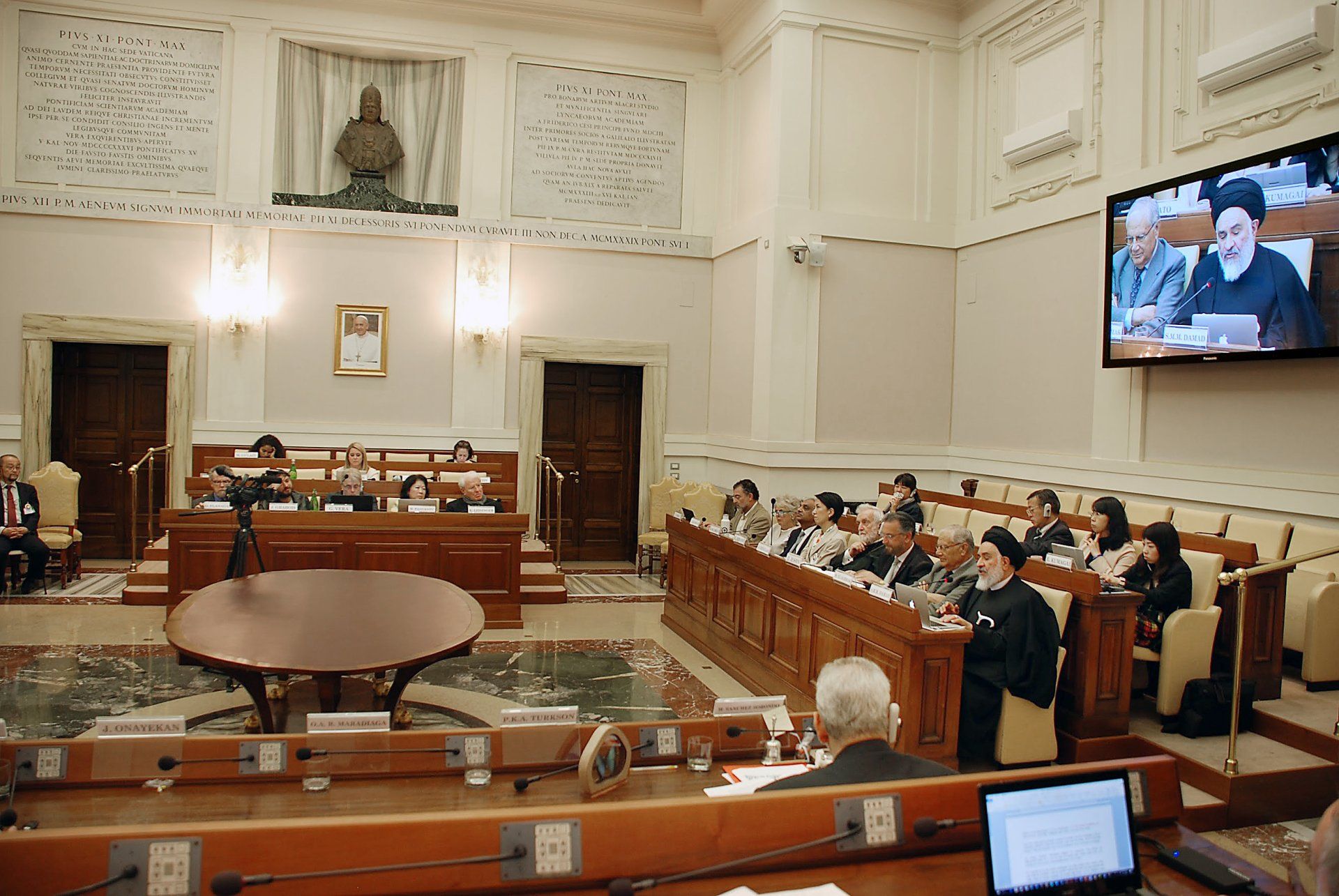 A group of people are sitting in front of a large screen in a room.