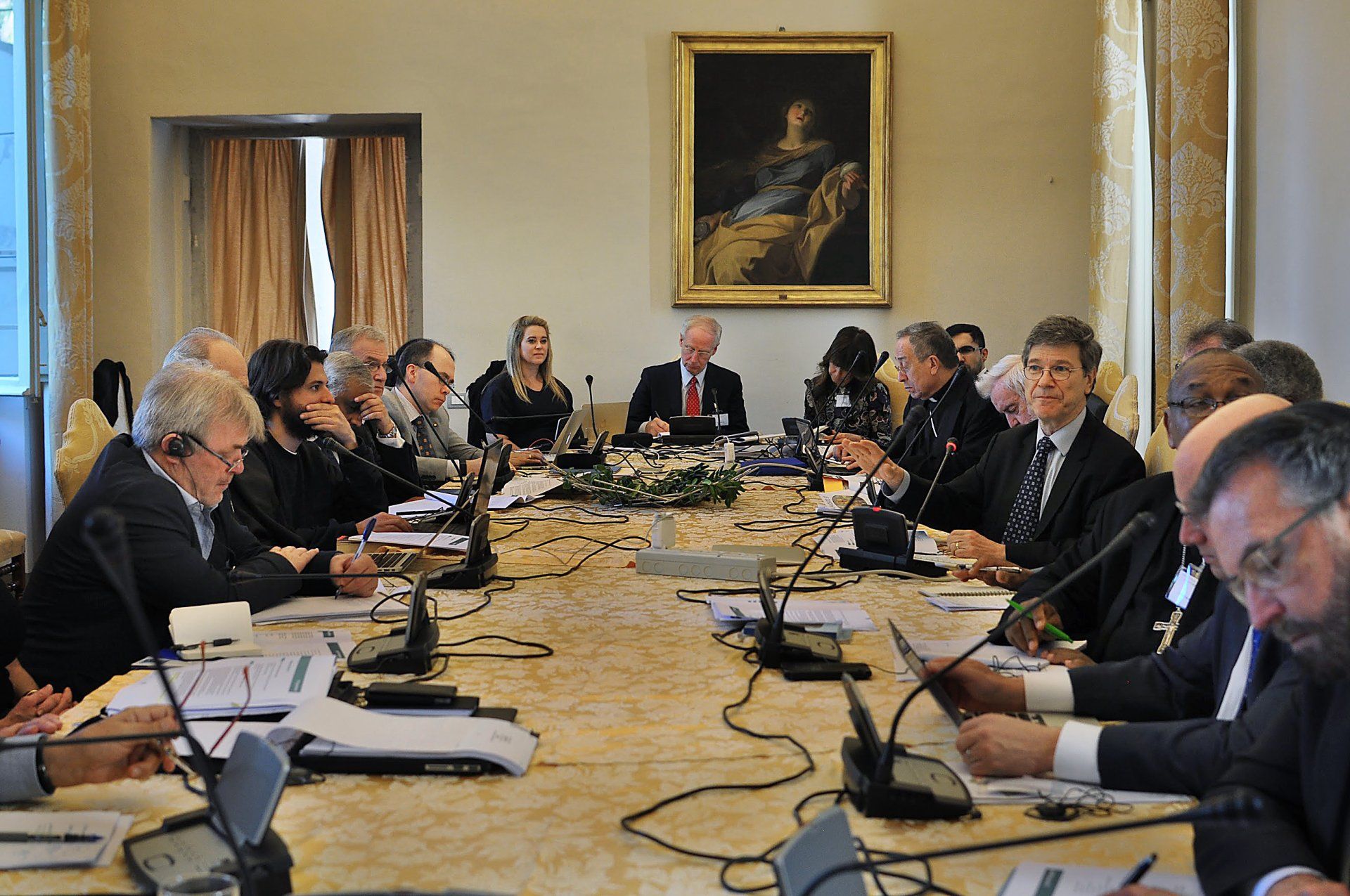 A group of people are sitting around a long table with microphones