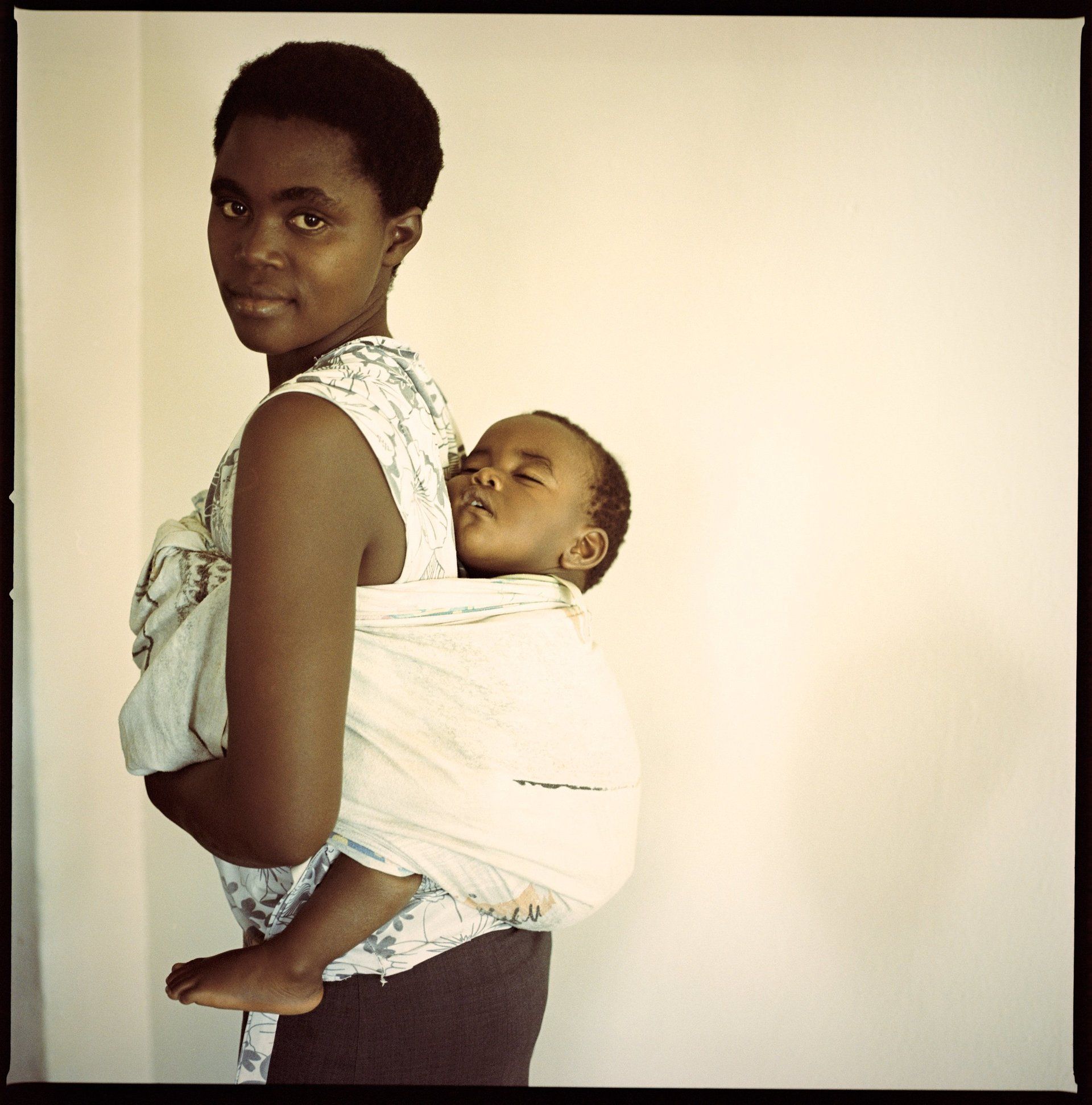 VII Foundation: A women standing sideways looking at the camera as a baby sleeps on her back