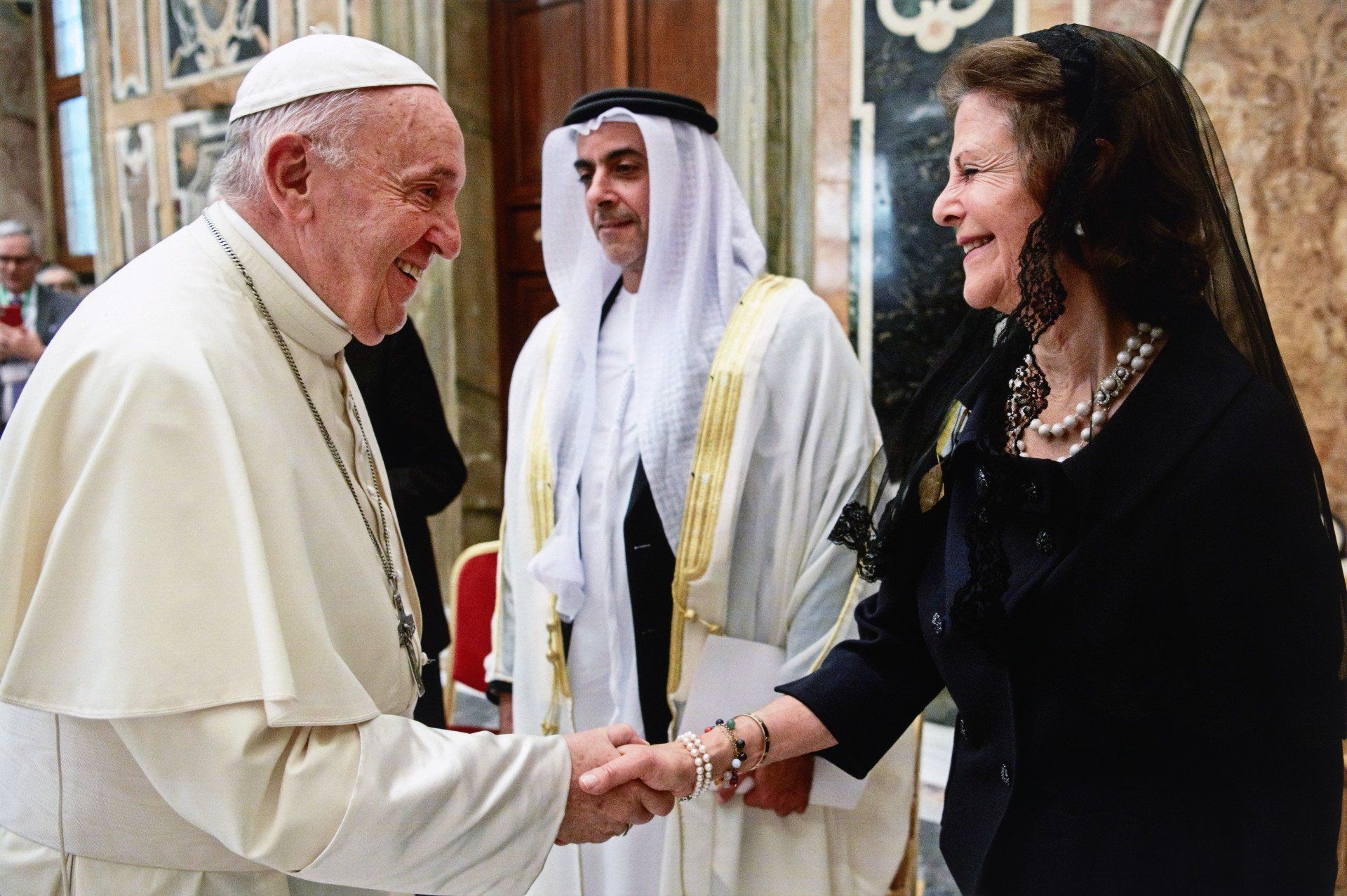 A man in a white robe is shaking hands with a woman