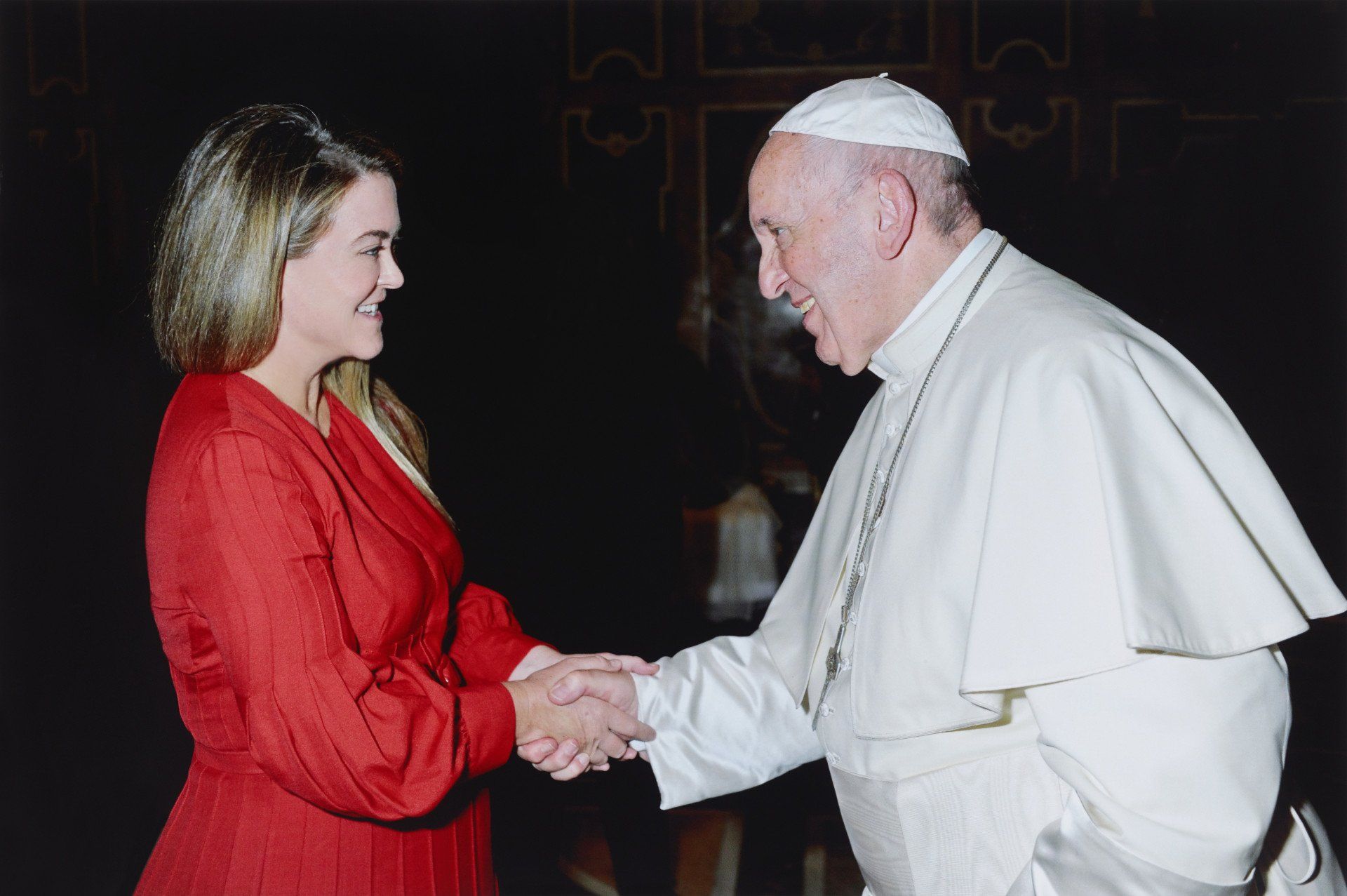 A woman in a red dress shakes hands with a man in a white robe