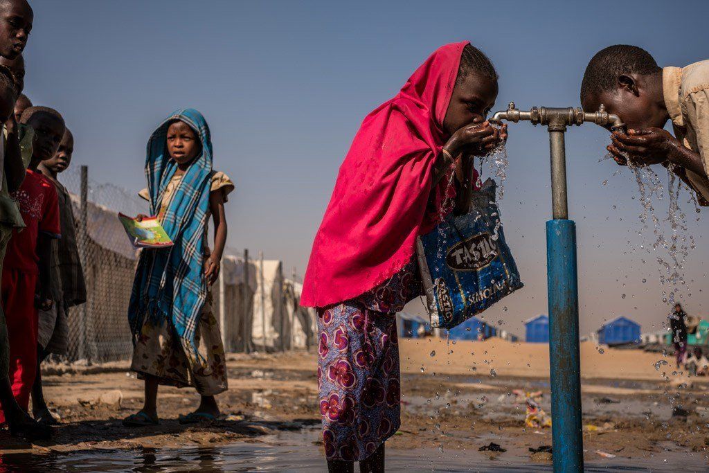A girl in a red cape is drinking water from a tap