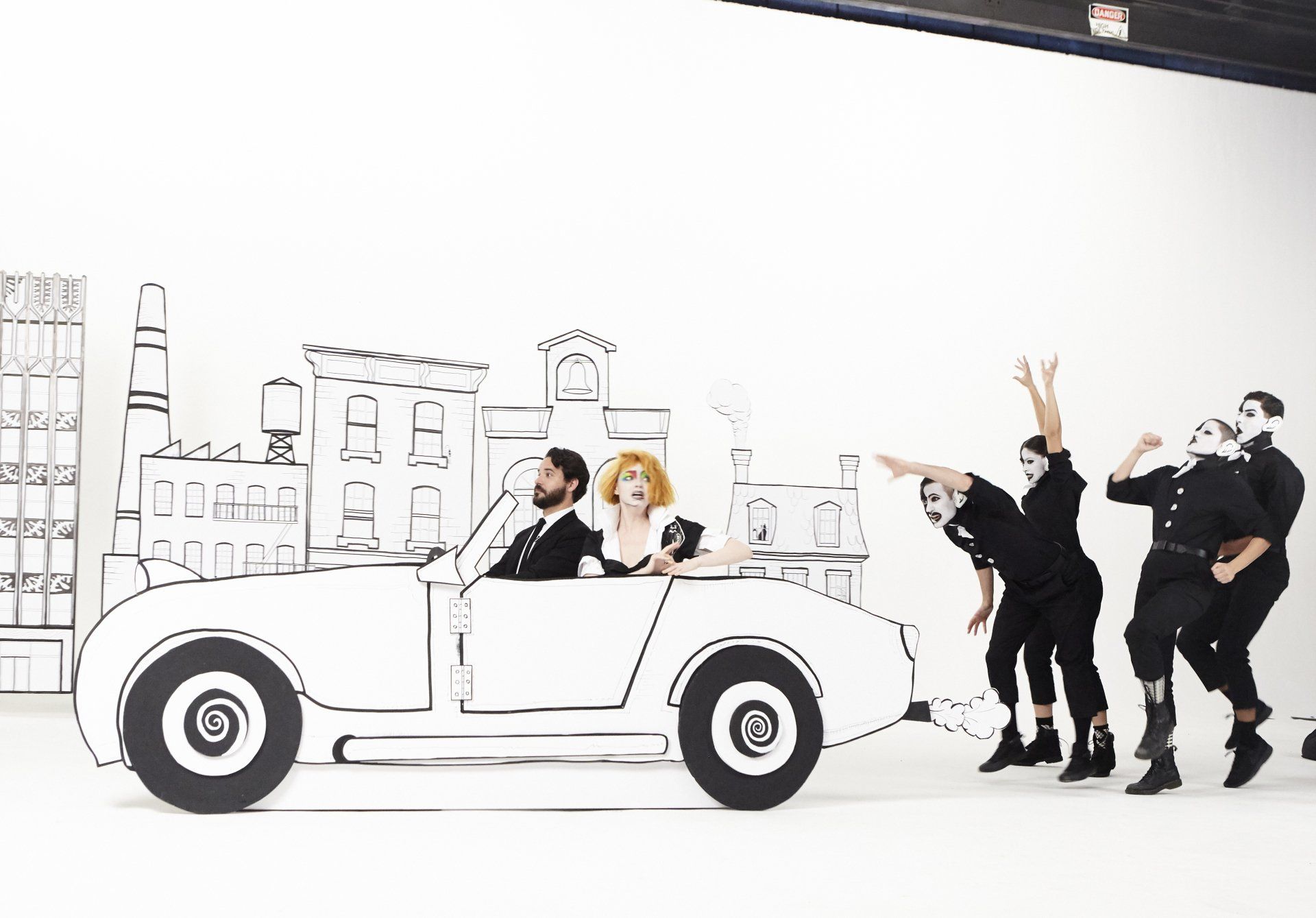 Who Cares set during the production, two people in a white paper car and others in all black following