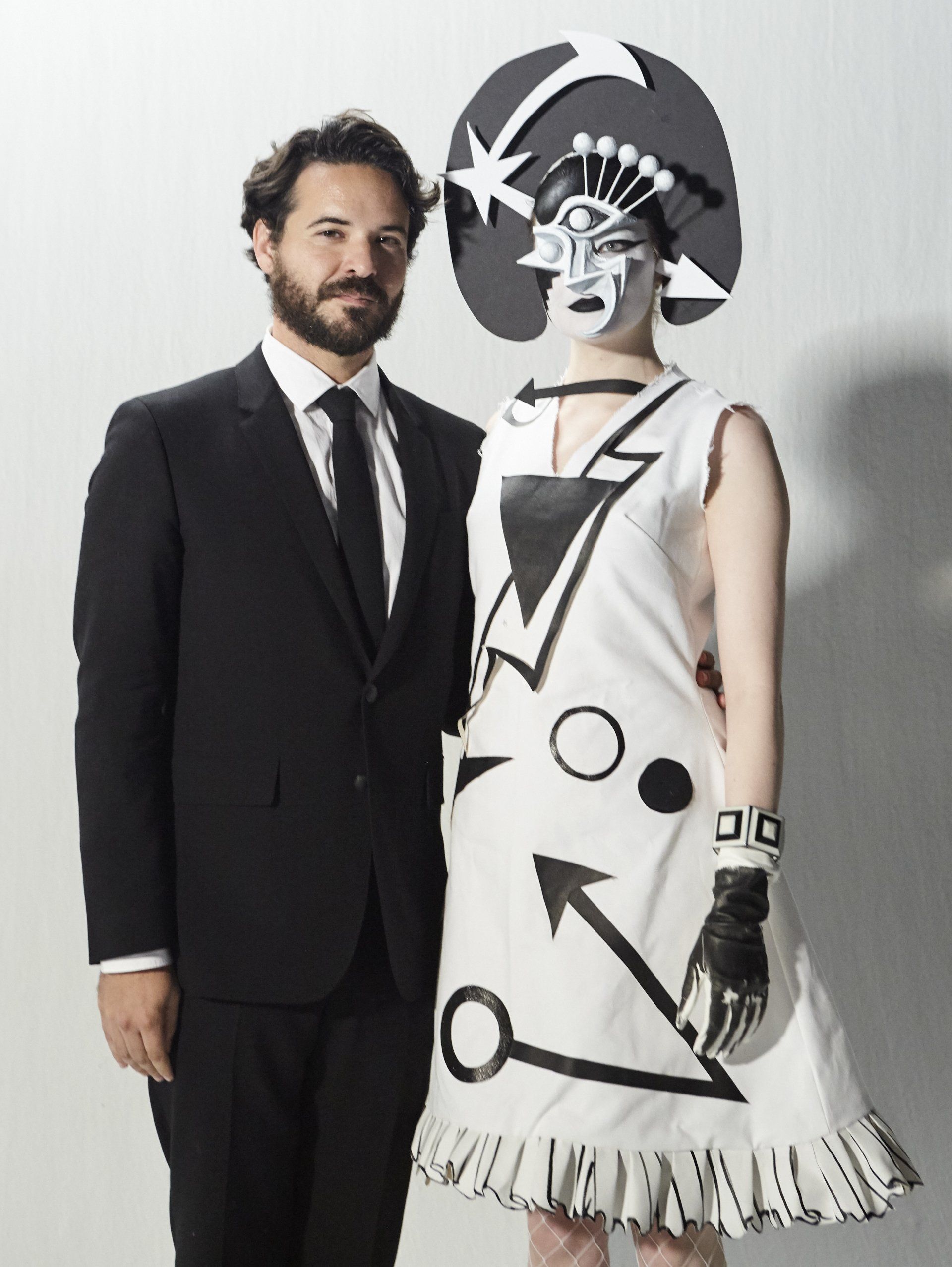 A man in a black suit and a women in a white dress with black shapes on it and a black and white head piece