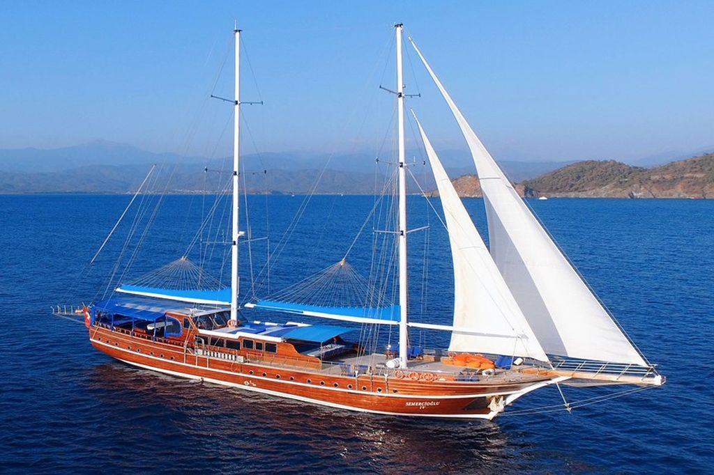 Grote houten zeilboot met witte zeilen op een blauwe zee.