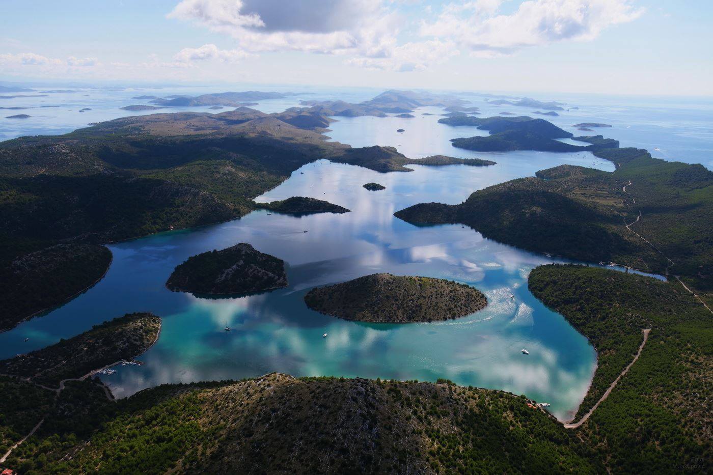 Luchtfoto van eilanden en turquoise water onder een blauwe hemel. Het land is bedekt met bos.