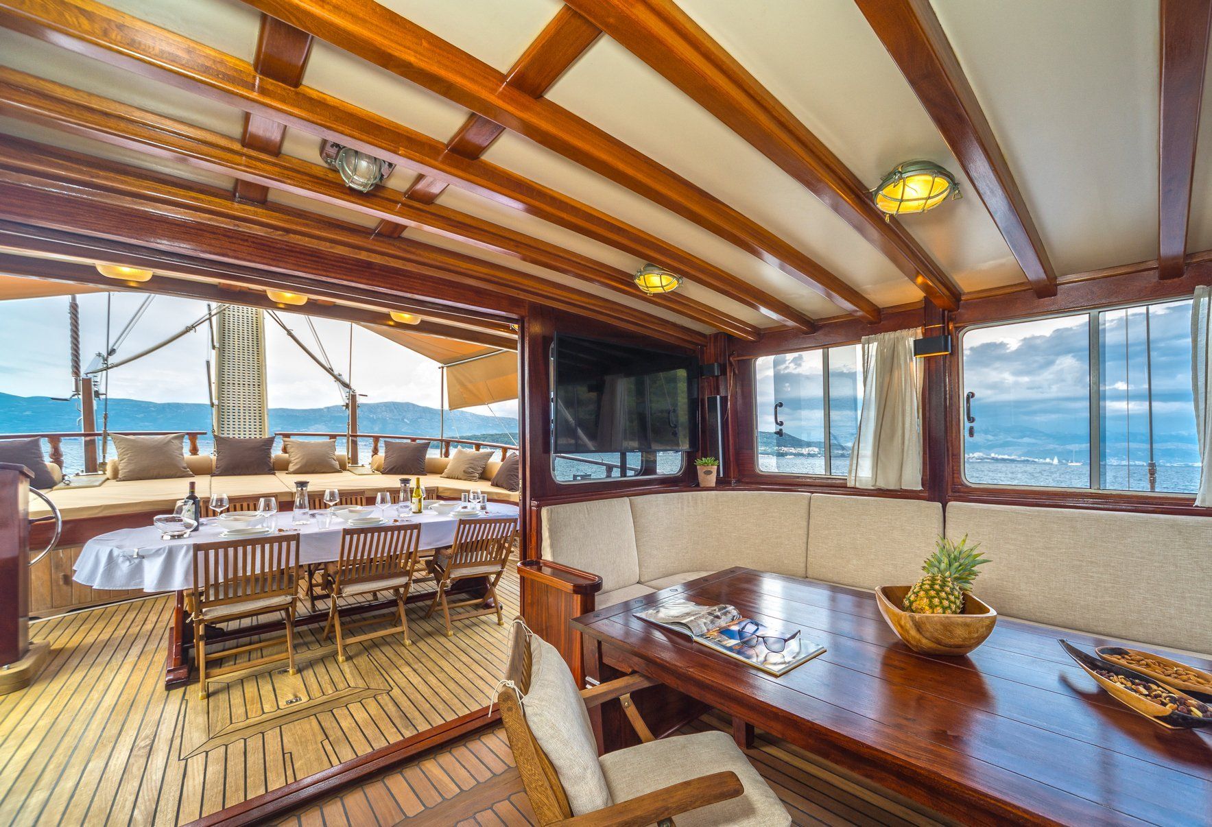 Interieur van een houten boot met eettafel, kussens en open zicht op de eethoek.