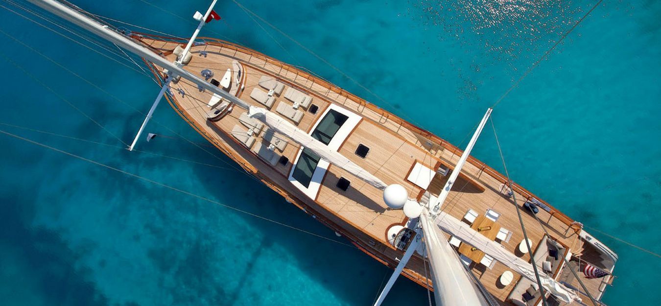 Luchtfoto van een houten zeilboot op turquoise water.