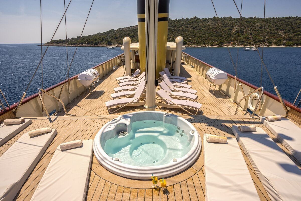 Houten jachtdek met jacuzzi, ligstoelen en uitzicht op zee.