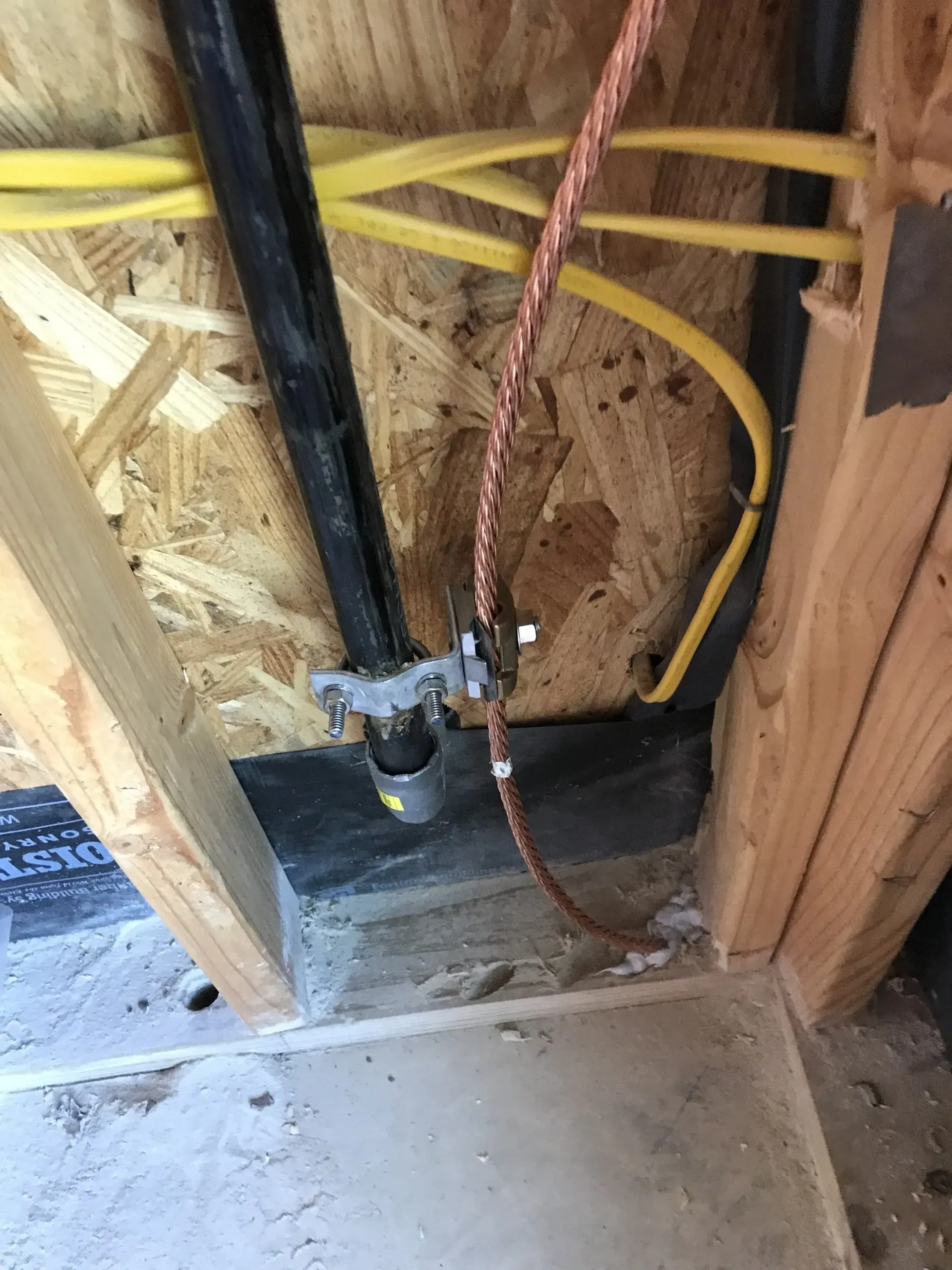 A copper wire is connected to a pipe in a wooden wall.