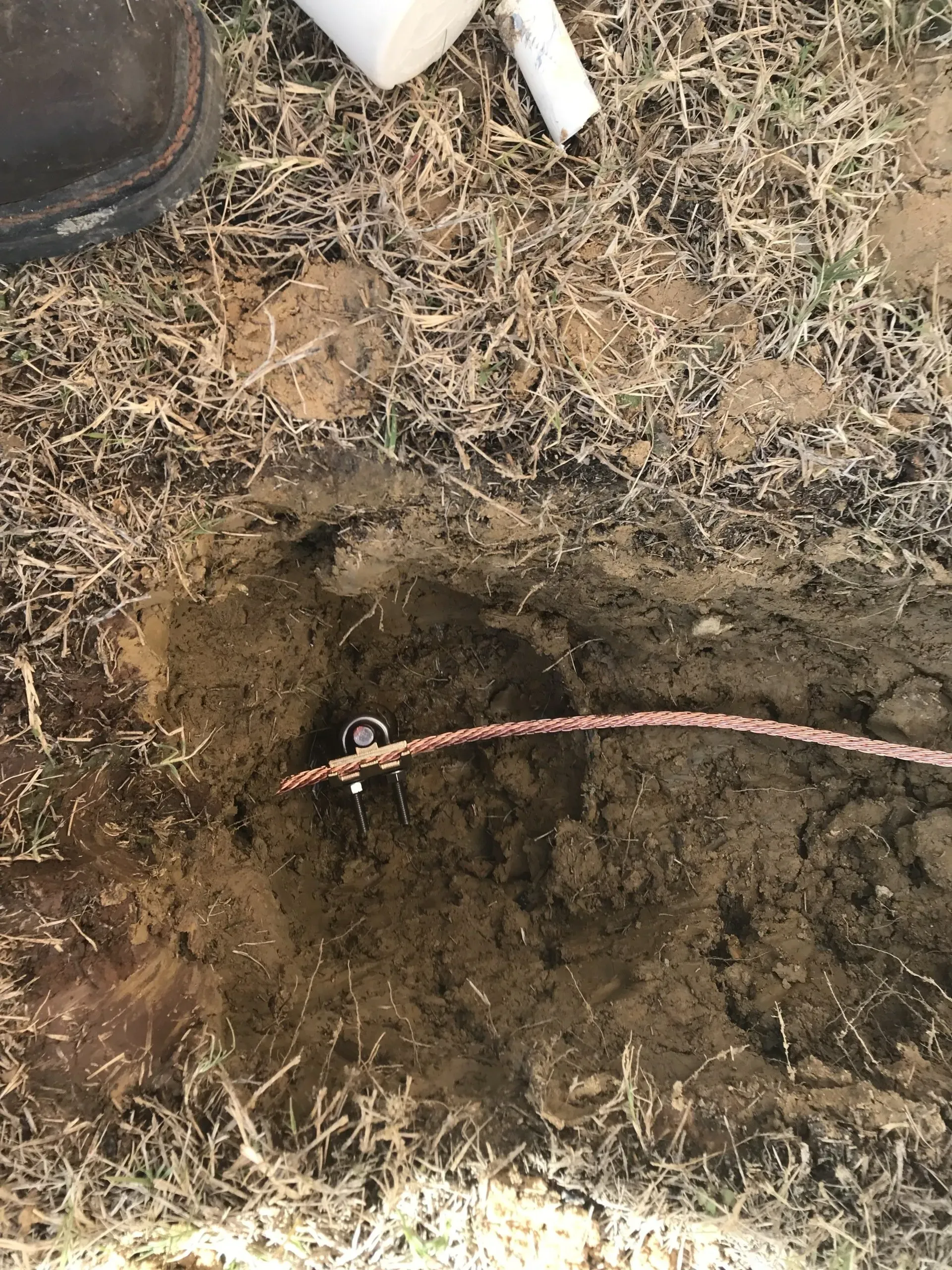 A person is digging a hole in the ground with a copper wire sticking out of it.