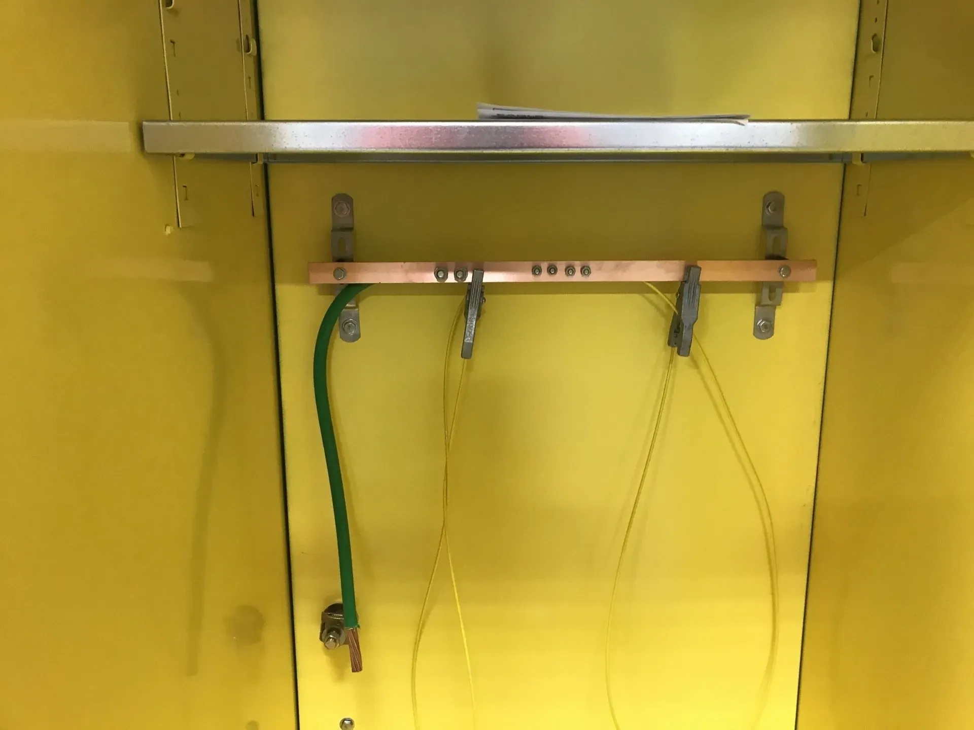 A yellow wall with a copper bar and a green wire attached to it.