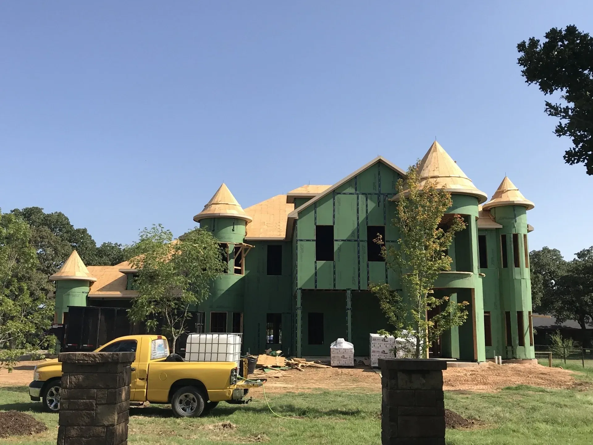 A yellow truck is parked in front of a large house under construction.