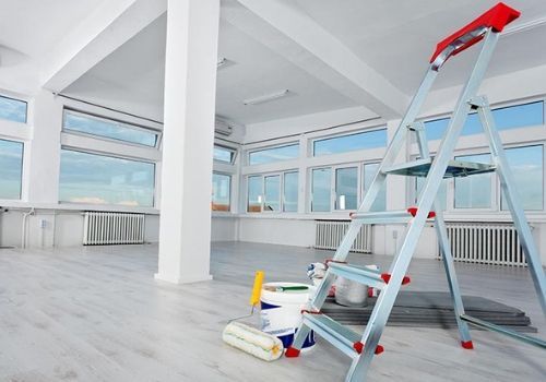 Interior room being renovated with a ladder, paint supplies, and large windows.