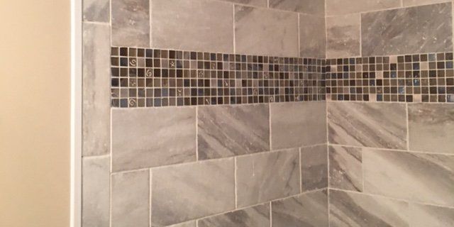 Gray marble tile wall with decorative mosaic accent.