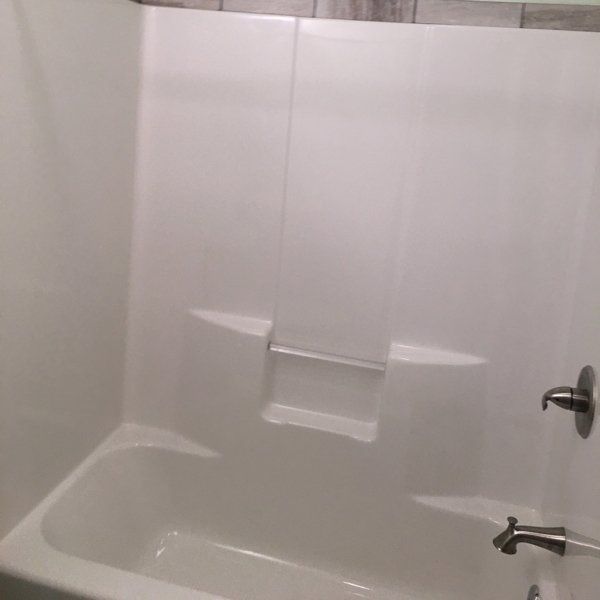 White bathtub shower combo with built-in storage shelves.