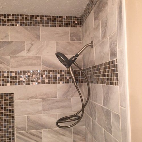 Shower with gray tiles and a mounted showerhead.