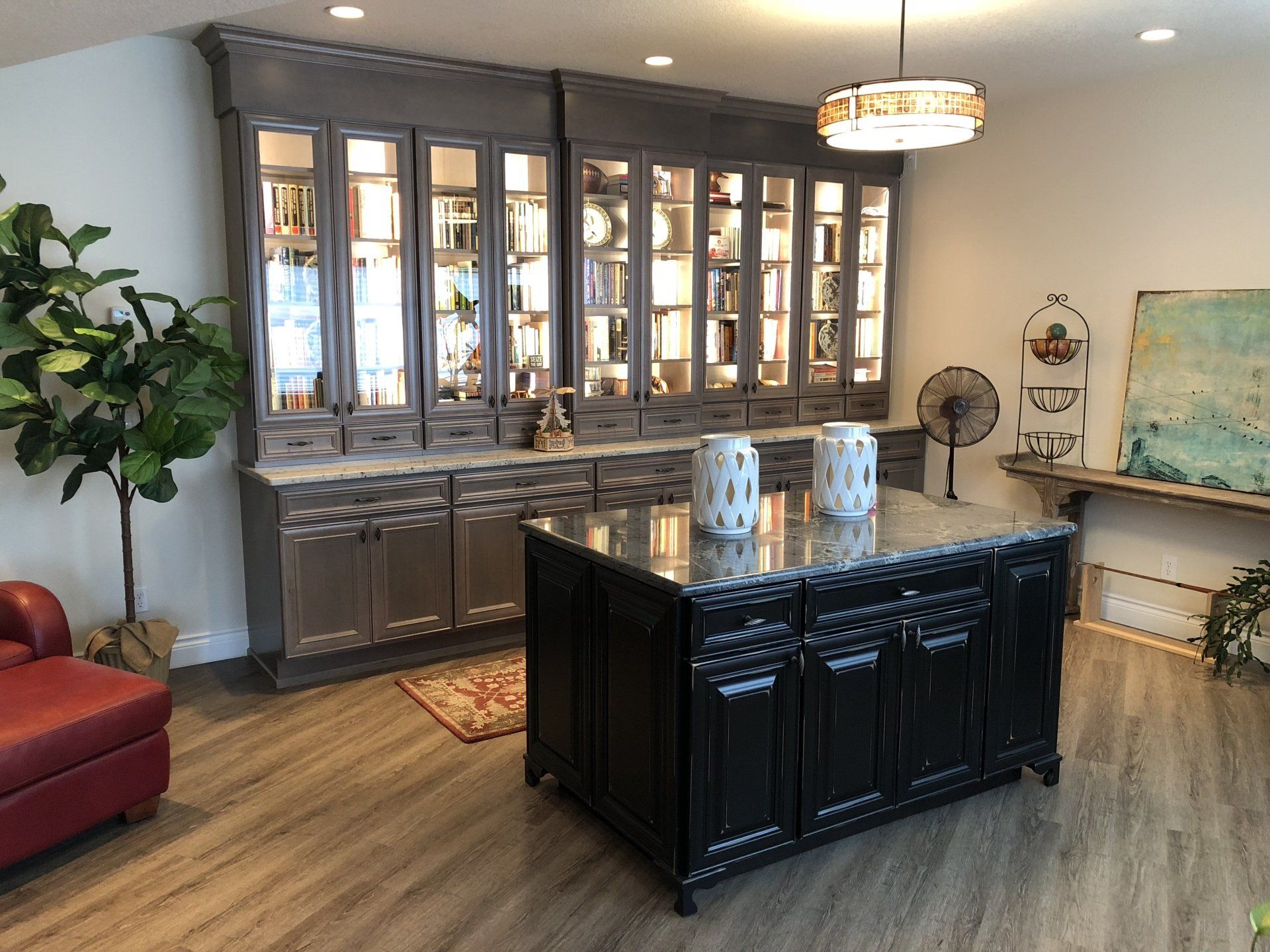 Modern showroom with a black display island, glass-front cabinets, red chair, and potted plant on wood flooring