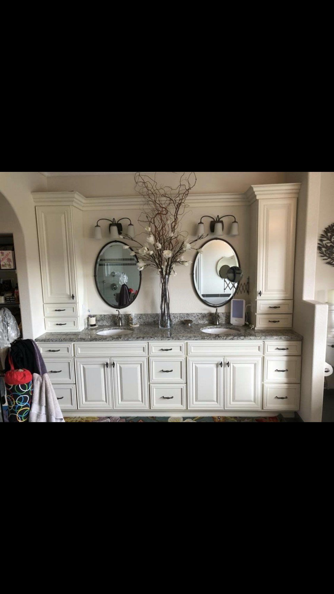 White bathroom vanity with two round mirrors, decorative branches, and cabinets in a bright beige room
