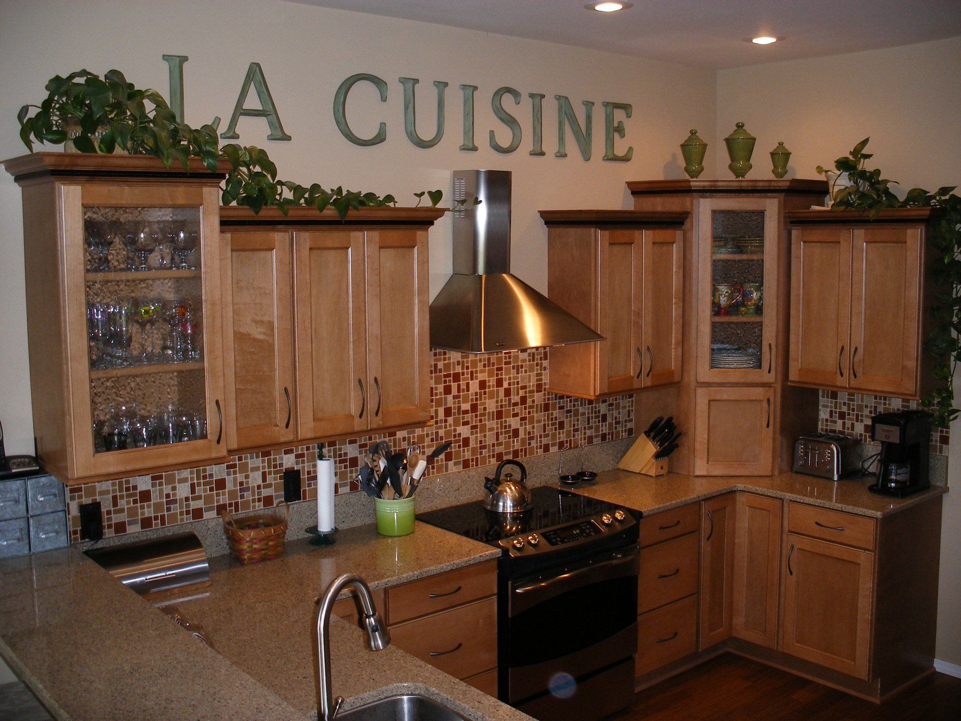 A cozy kitchen with wooden cabinets, granite counters, a stainless steel stove hood, and decorative glass-front cupboards.