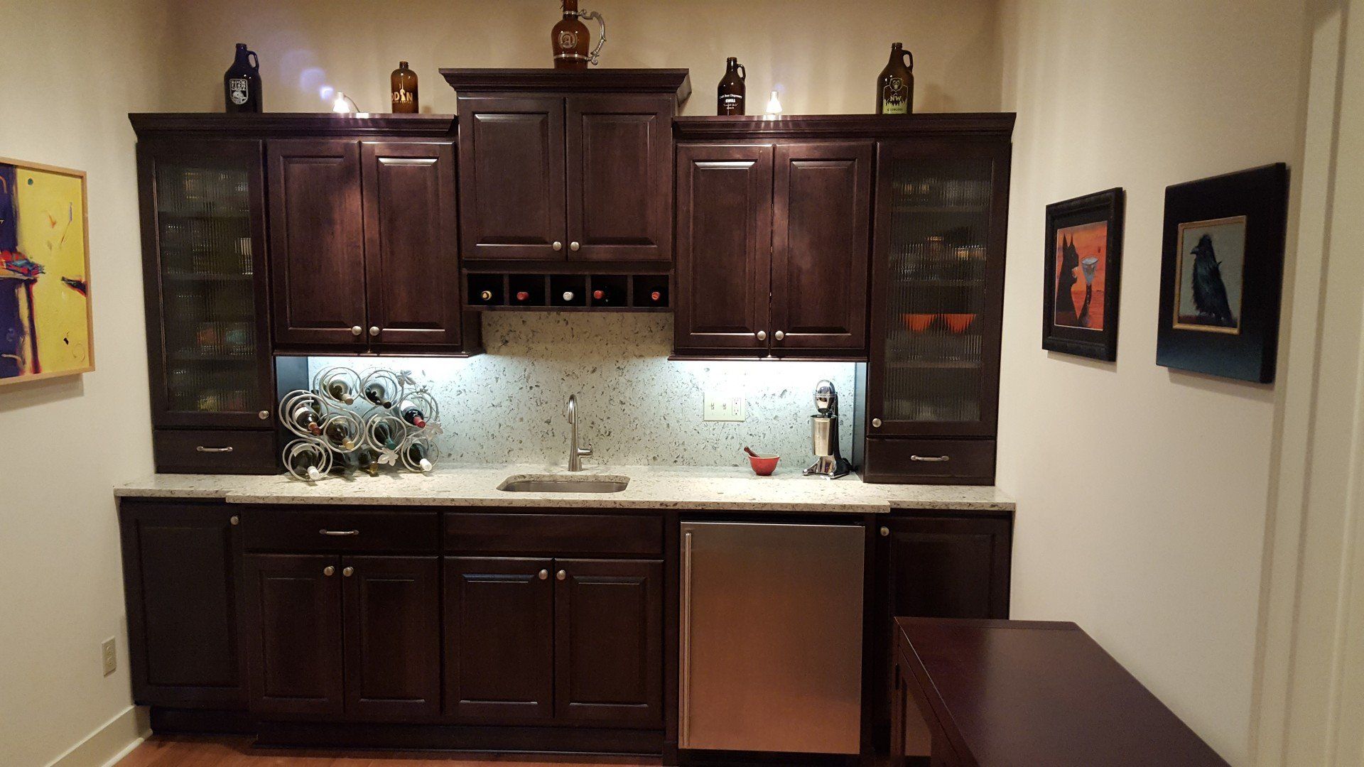 Dark wood kitchen cabinets and countertop with under-cabinet lighting, stainless appliance, and wall art.