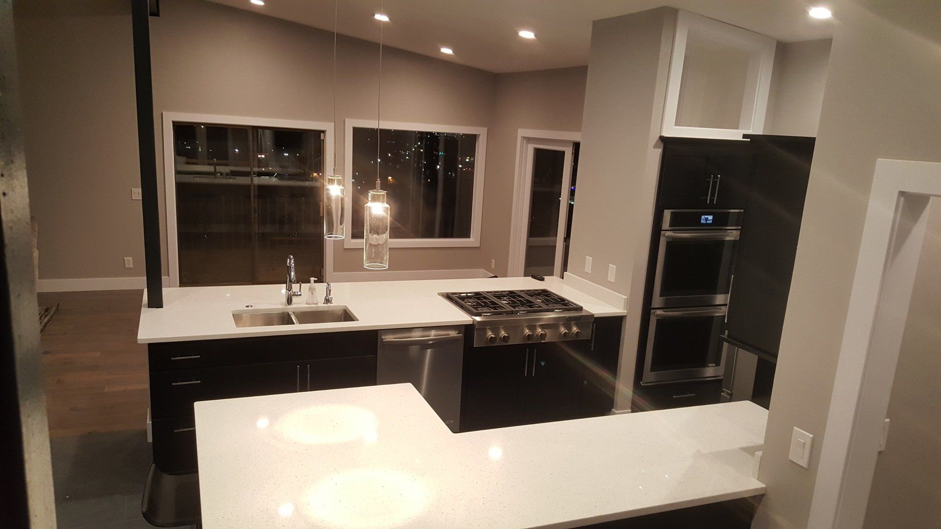 Modern kitchen with dark cabinets, white countertops, island, and stainless steel appliances at night