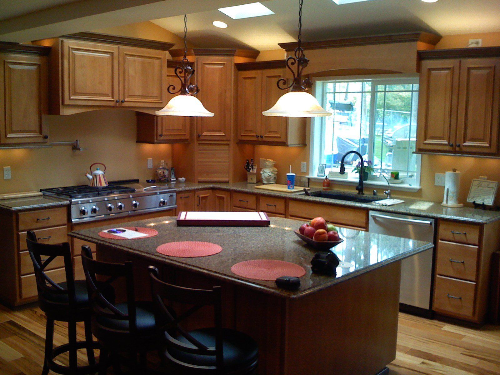 Warm kitchen with wooden cabinets, black island, pendant lights, stove, sink, and window over the counter