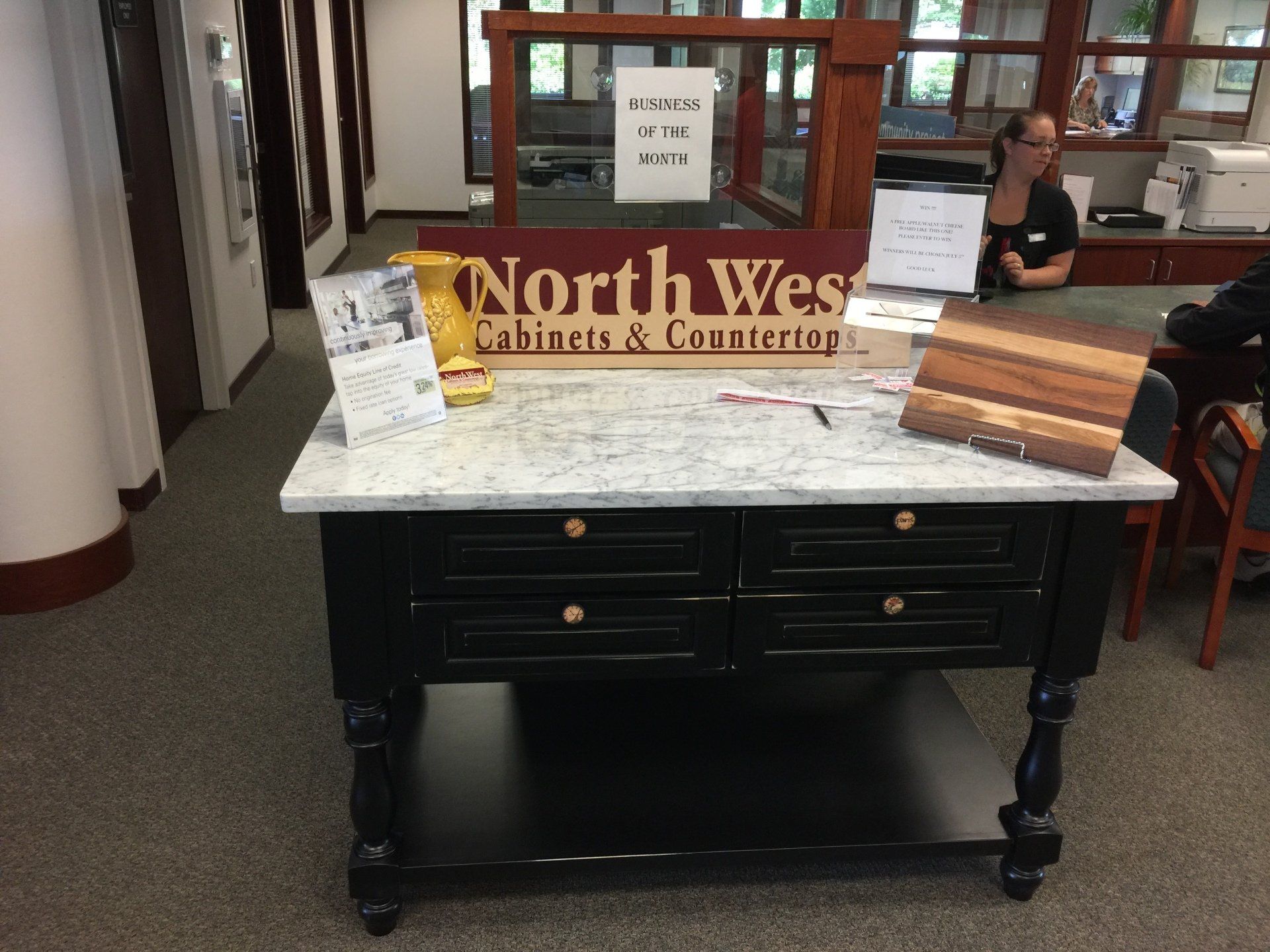Black console table with white marble top displayed in a showroom, with a North West Cabinets & Counters sign behind it