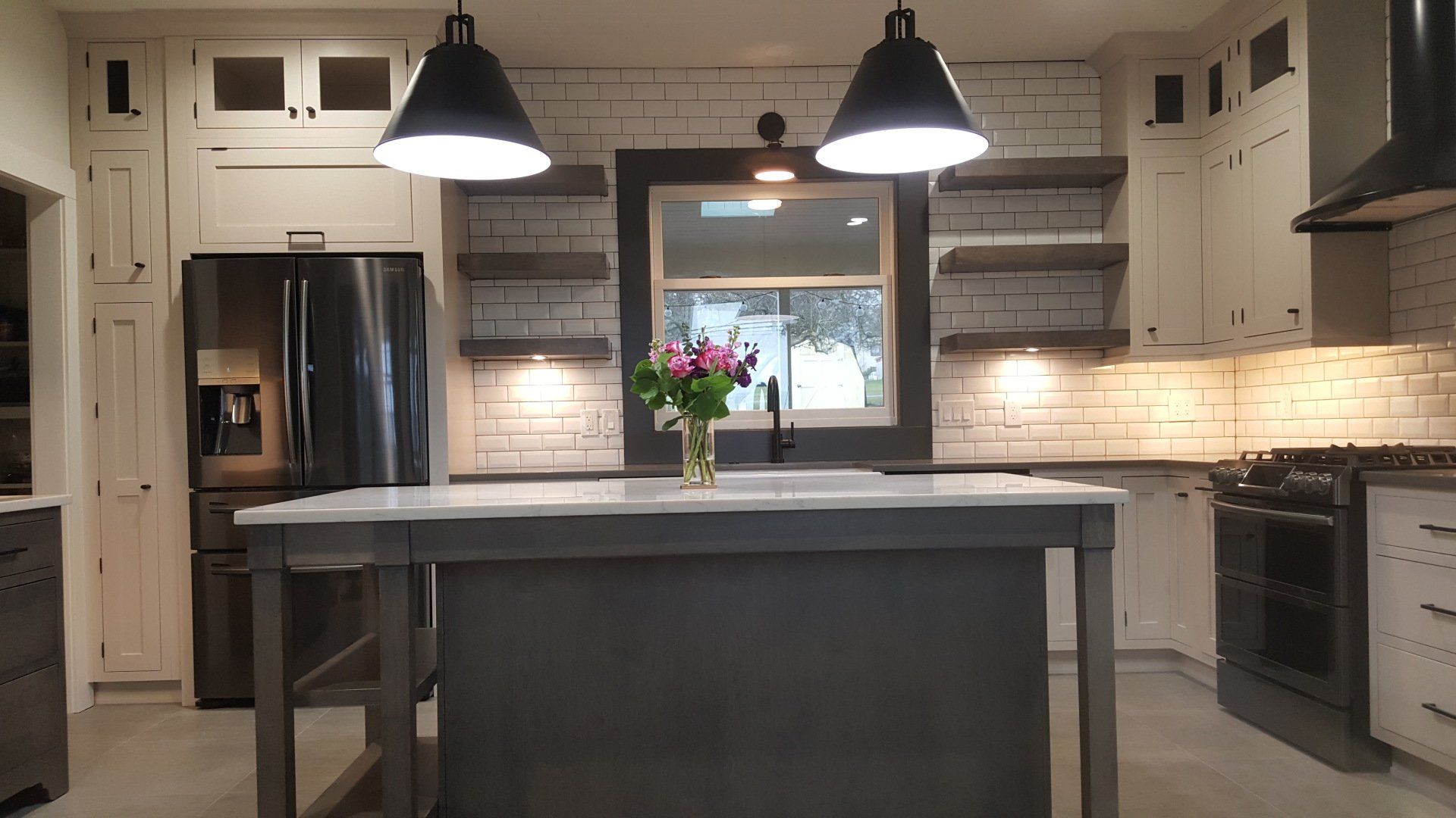 Modern kitchen with a central island, two pendant lights, stainless appliances, and a vase of flowers.