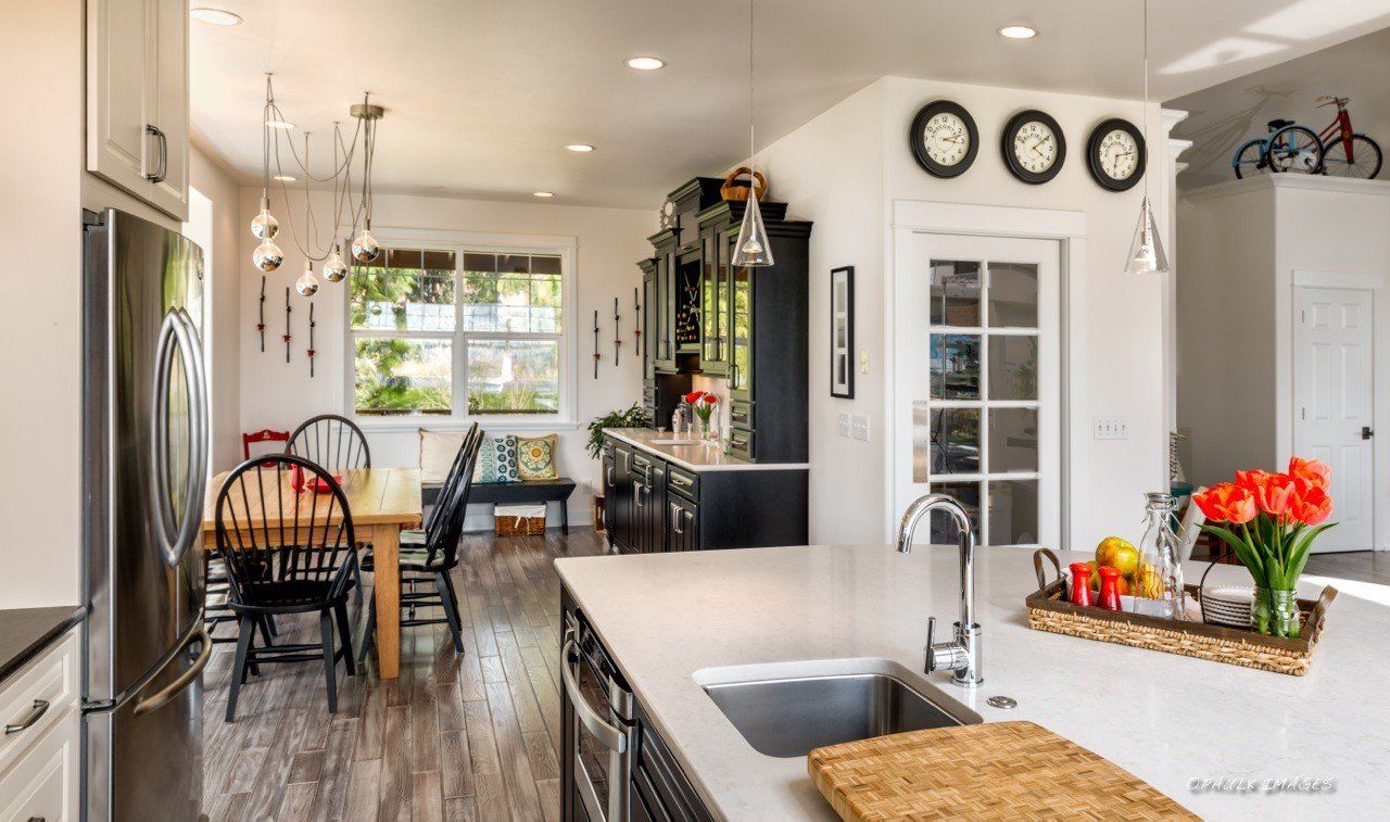 Bright kitchen with island sink, dining table, pendant lights, and flowers near a window.