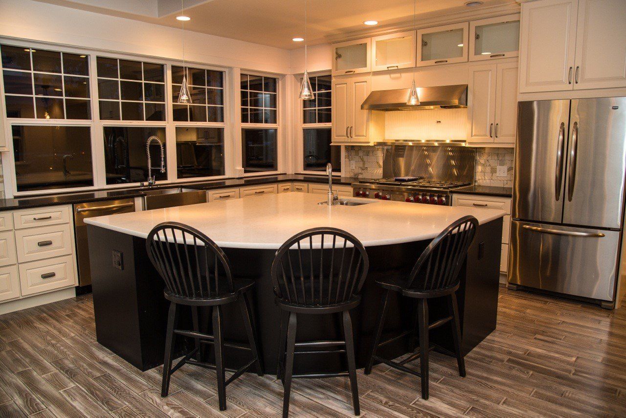 Modern kitchen with large island, black chairs, stainless steel appliances, and warm under-cabinet lighting.