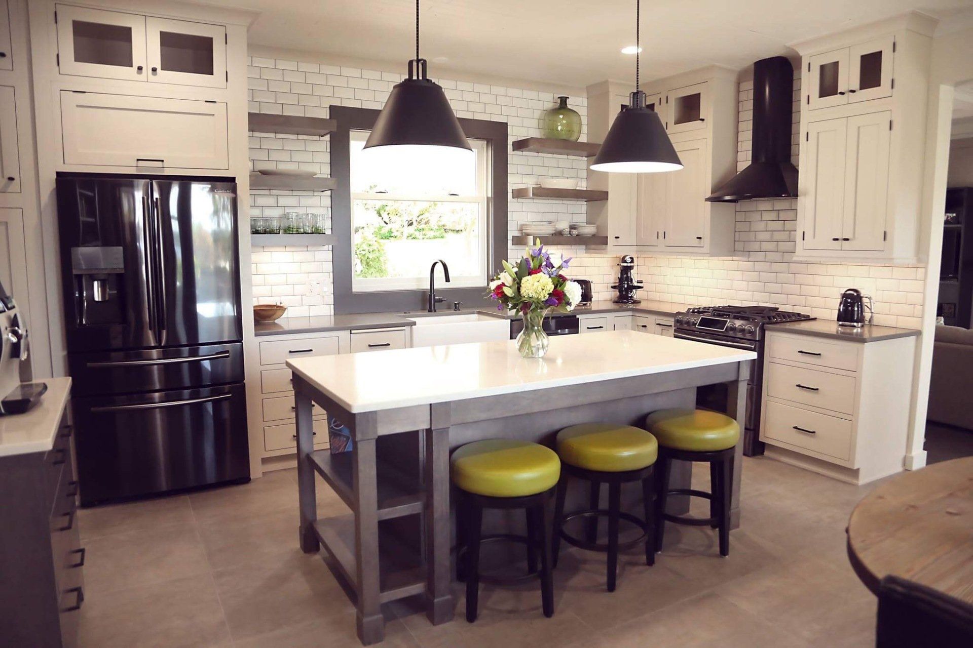 Modern kitchen with black appliances, white cabinets, island, pendant lights, and three green stools