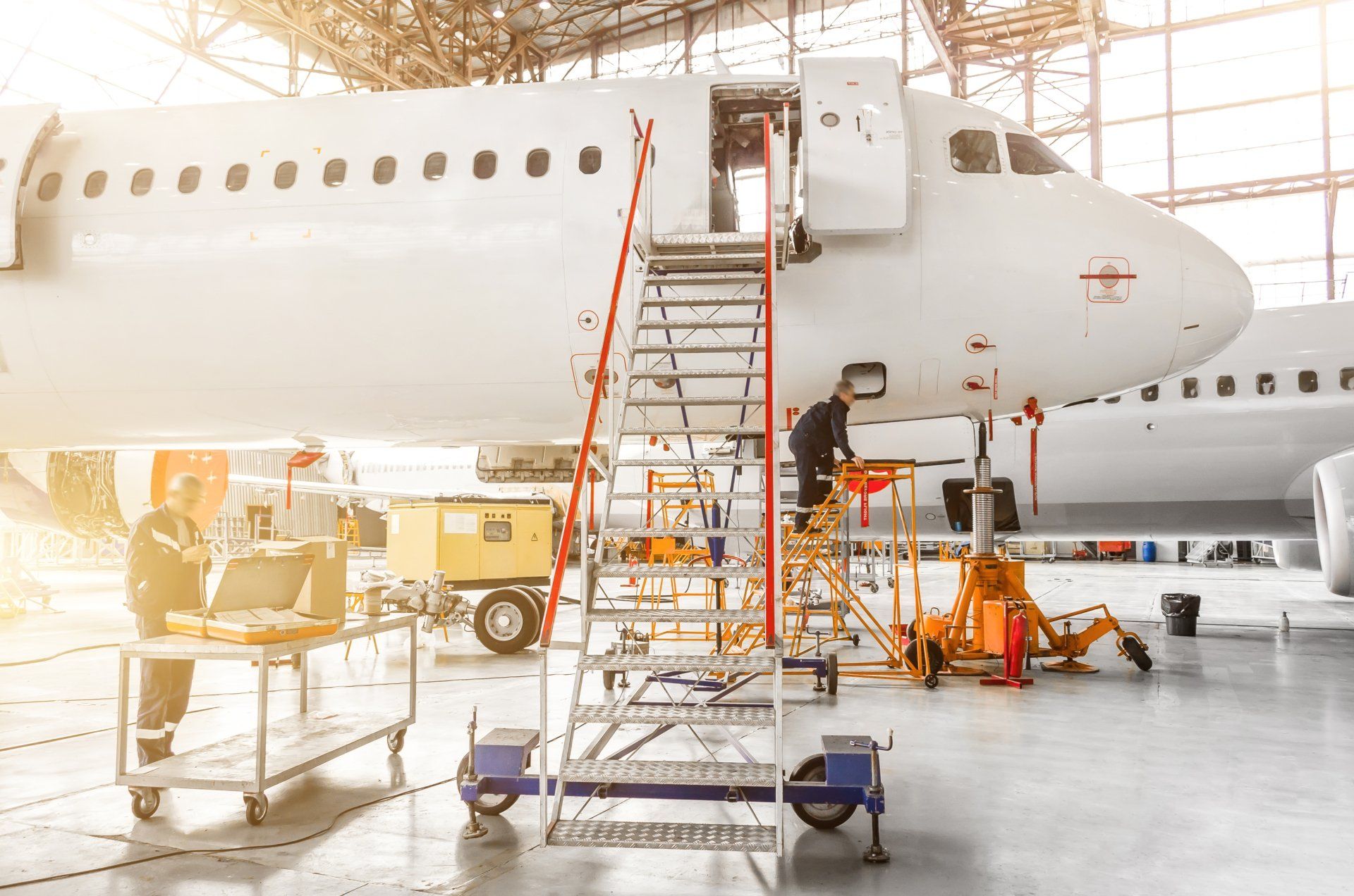 Large white airplane in a hangar with maintenance stairs and equipment around it