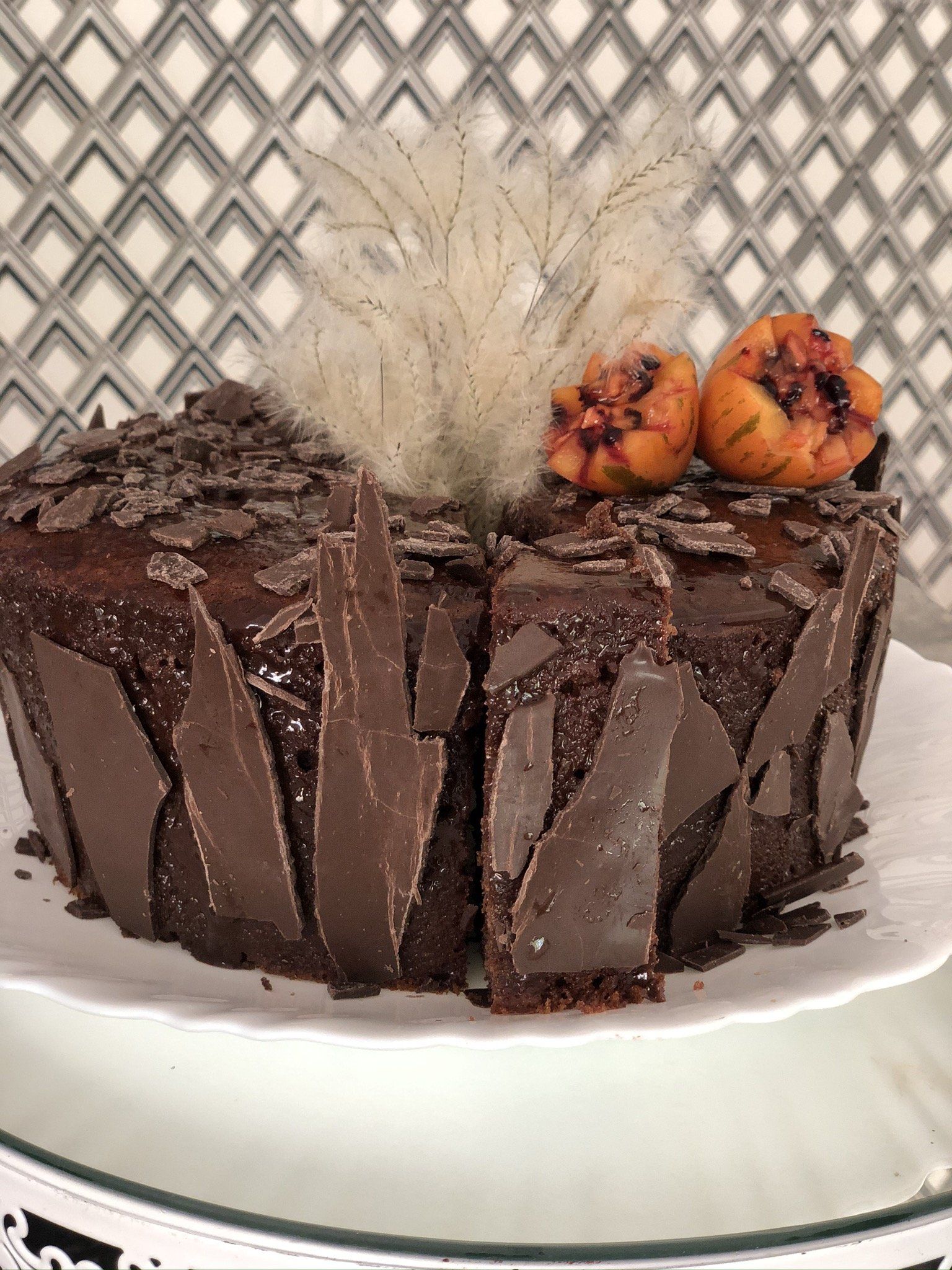 Um bolo de chocolate com raspas de chocolate e abóboras no topo está em um prato branco.