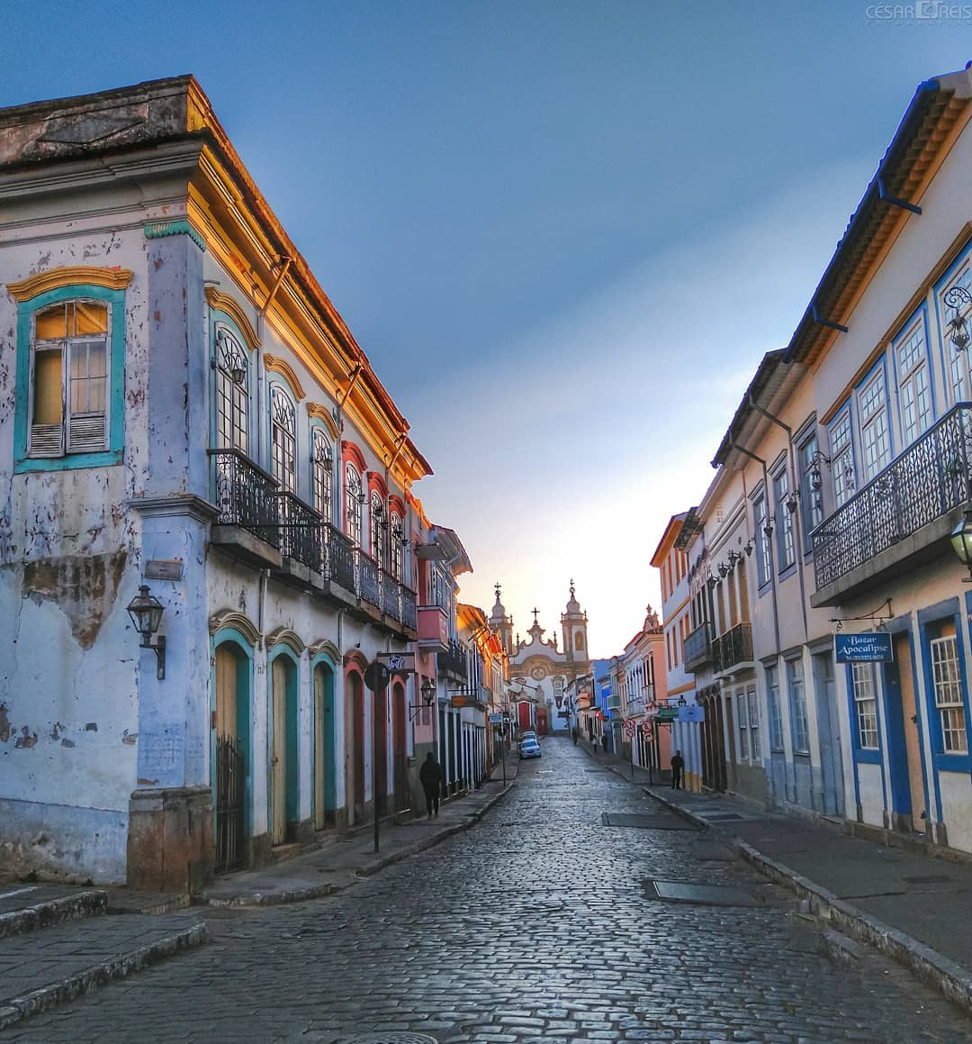 Uma rua de paralelepípedos com prédios em ambos os lados e uma torre do relógio ao fundo