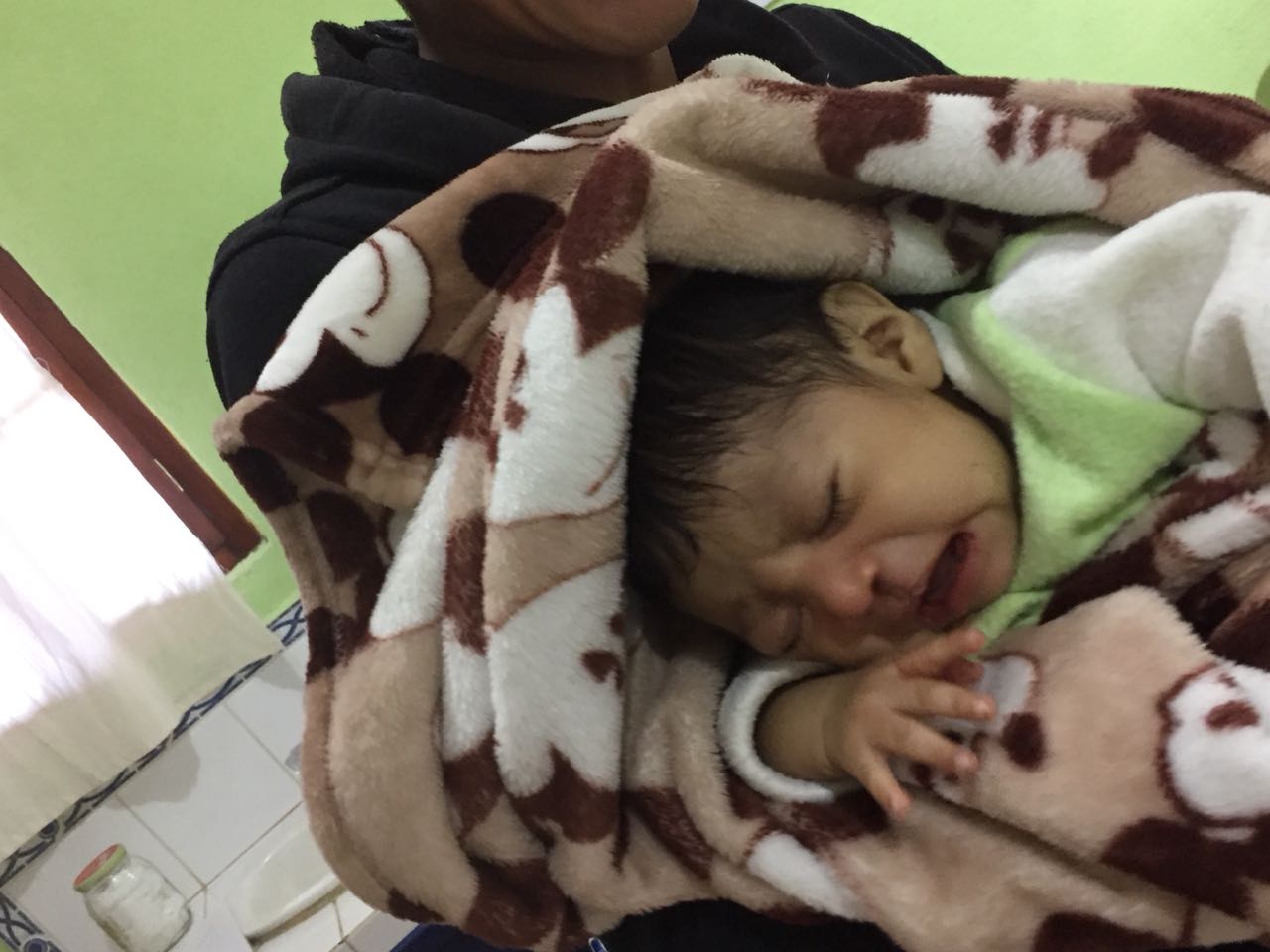 Eine Person hält ein weinendes Baby, das in eine braun-weiße Decke gewickelt ist.