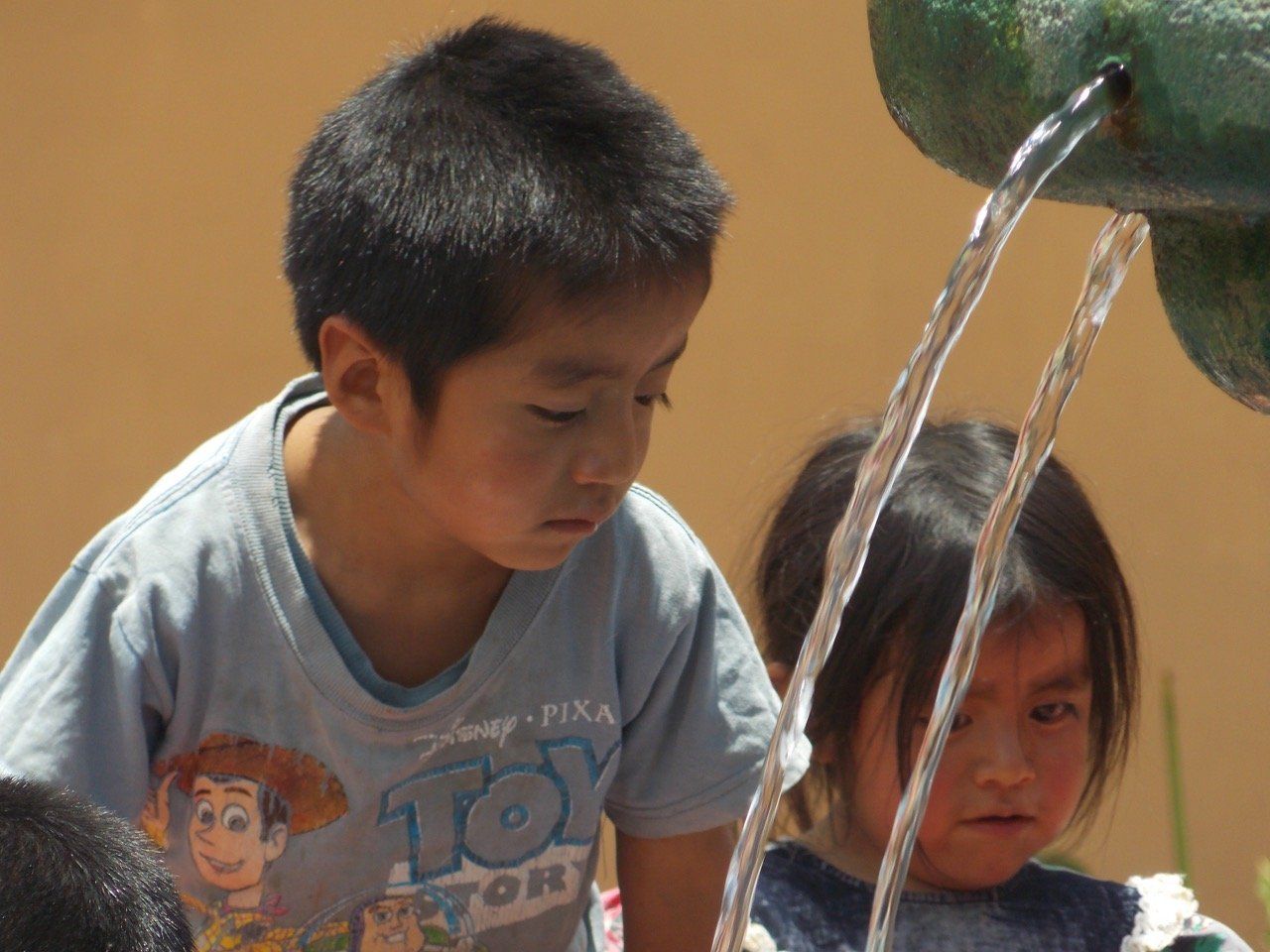 Zwei Kinder beobachten, wie Wasser aus einem Springbrunnen fließt;