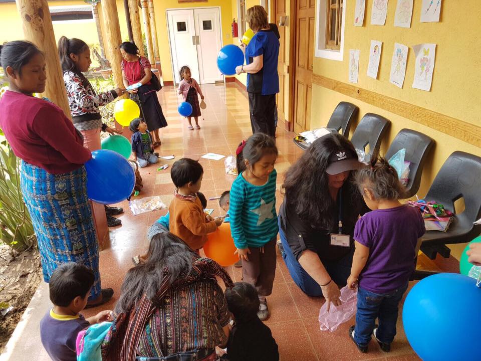 Menschen und Kinder spielen in einem Flur mit Luftballons. Einige Erwachsene beobachten die Kinder.