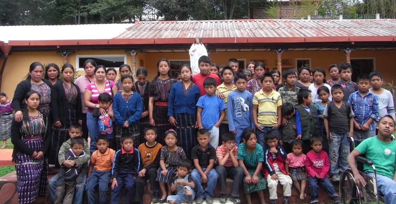 Eine Gruppe von Menschen posiert vor einem Gebäude für ein Foto; viele Kinder, einige in bunter Kleidung, lächeln.