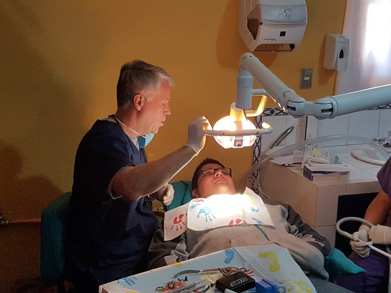 Ein Zahnarzt untersucht den Mund eines Patienten unter hellem Licht in einer Zahnarztpraxis.