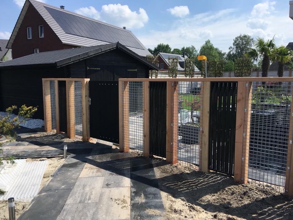 Een schutting met afwisselende secties van houten palen, gaas en zwarte verticale latten leidt naar een bijpassende tuinpoort.
