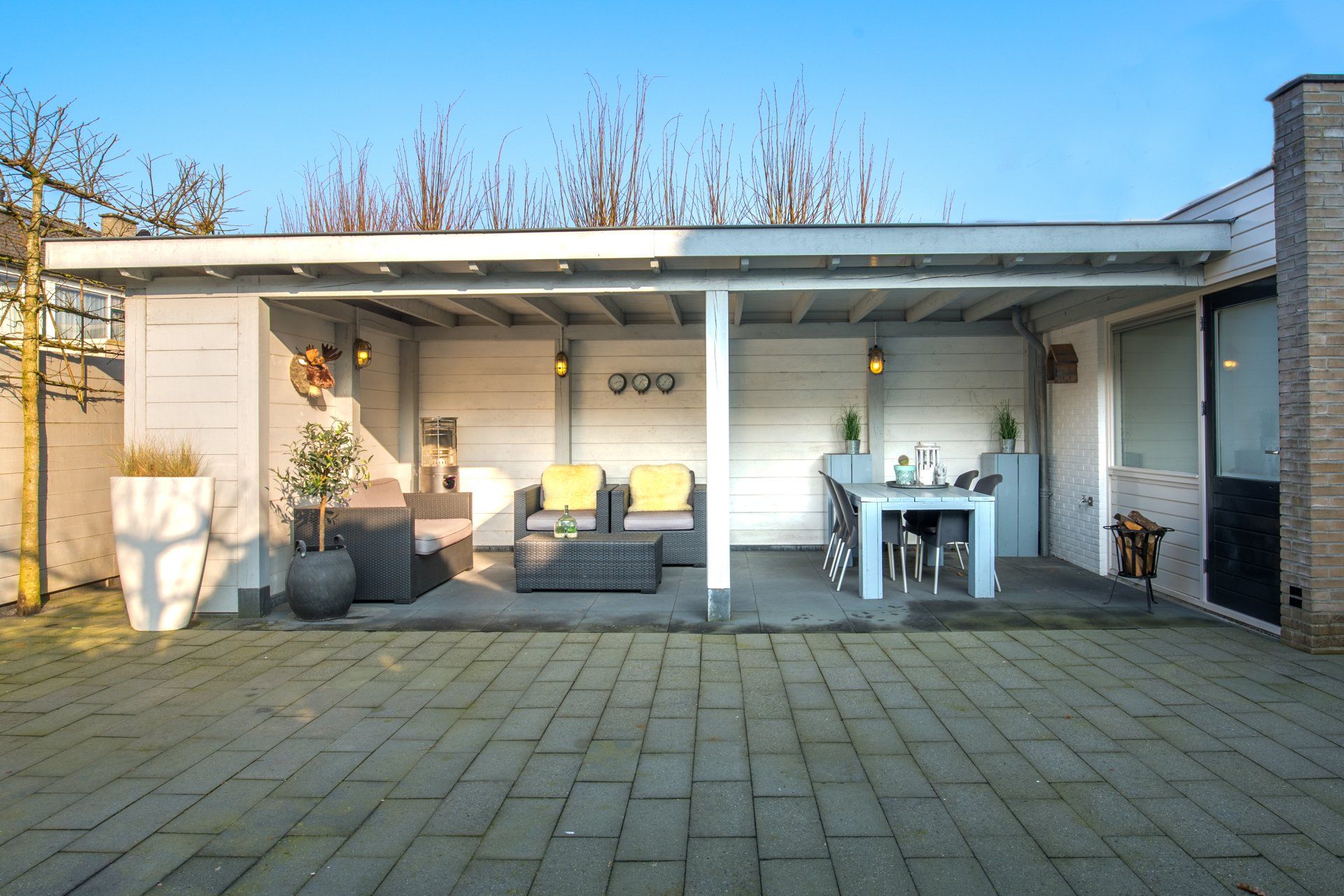 Een moderne overdekte patio met grijze muren, een loungeset voor buiten en een eethoek op een betegeld terras in de achtertuin.