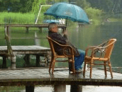 Ein Mann sitzt auf einem Dock und hält einen Regenschirm.
